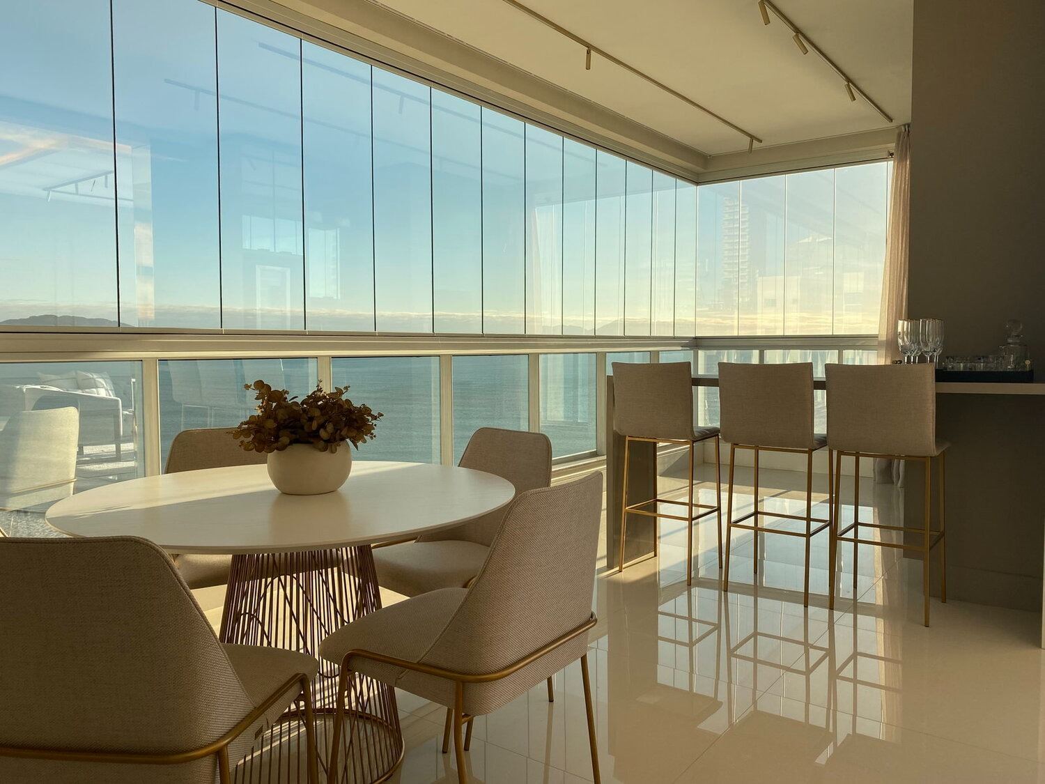 Varanda gourmet com mesa posta e vista panorâmica para o mar ao entardecer, apartamento mobiliado na Meia Praia, Itapema